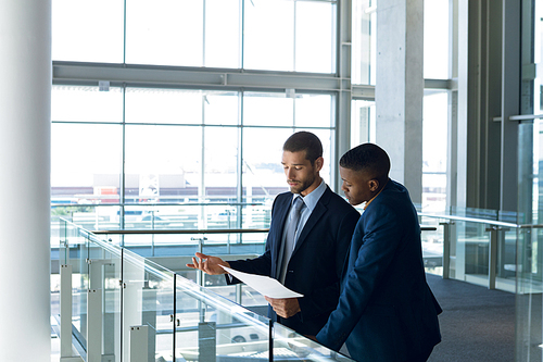 Side view of a young African American businessman  talking with a young Caucasian businessman holding documents standing in the lobby of a modern business building. Modern corporate start up new business concept with entrepreneur working hard