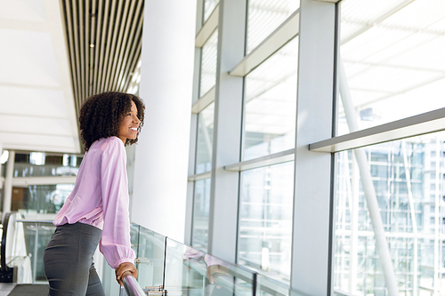Side view of young African American businesswoman looking out of window standing in modern business lobby. Modern corporate start up new business concept with entrepreneur working hard
