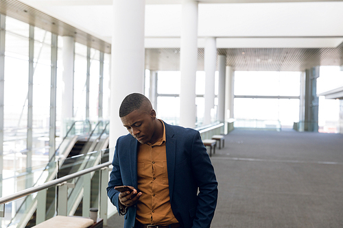 Front view of young African American businessman using smartphone in the glass walled lobby of a modern business building. Modern corporate start up new business concept with entrepreneur working hard