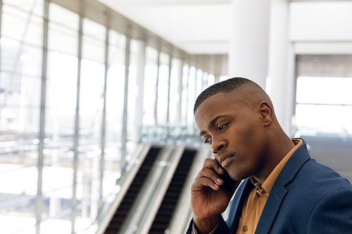 Close up side view of young African American businessman making a phone call on a smartphone in the glass walled lobby of a modern business building. Modern corporate start up new business concept with entrepreneur working hard