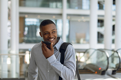 Close up portrait of smiling young African American businessman talking on his smartphone in the lobby of a modern building with a shoulder bag. Modern corporate start up new business concept with entrepreneur working hard