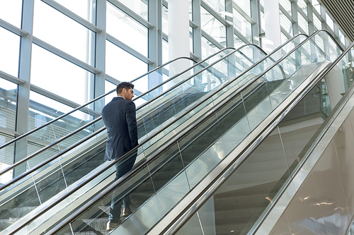 Full length rear view of young Caucasian businessman going up an escalator in a modern office building. Modern corporate start up new business concept with entrepreneur working hard