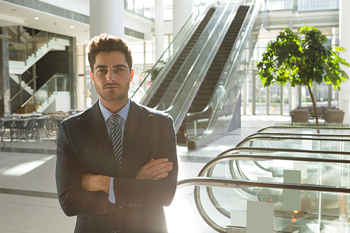 Portrait of young Caucasian businessman looking to camera with arms crossed, standing in the atrium of modern business. Modern corporate start up new business concept with entrepreneur working hard