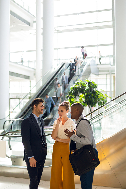Front view of a young African American businessman talking with a young Caucasian businessman and businesswoman in the atrium of a busy modern building. Modern corporate start up new business concept with entrepreneur working hard