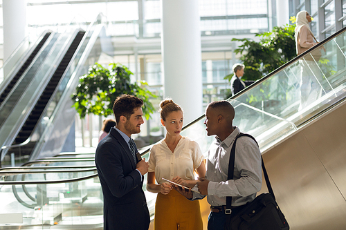 Front view of a young African American businessman holding tablet computer and talking with a young Caucasian businessman and businesswoman while in the lobby of a modern building. Modern corporate start up new business concept with entrepreneur working hard