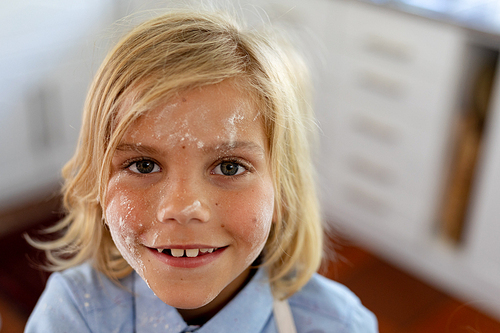 Portrait of a happy young blonde haired Caucasian boy smiling to camera with flour on his face while making cookies at Christmas time in his kitchen