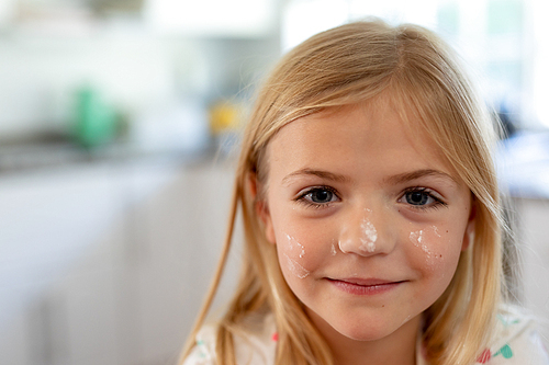 Portrait of a happy young blonde haired Caucasian girl smiling to camera with flour on her face while making cookies at Christmas time in her kitchen