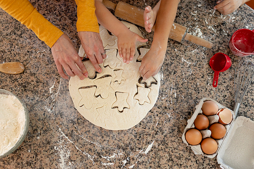 Overhead view of the hands of young Caucasian mother and her son and daughter in their kitchen at Christmas time making cookies, cutting out shapes in dough with cookie cutters on a kitchen worktop
