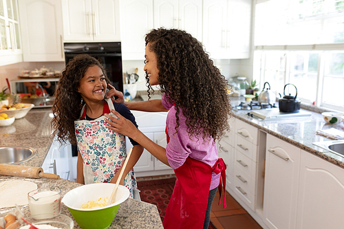 Side view of a mixed race woman in a kitchen with her young daughter at Christmas, making cookies, facing each other and smiling