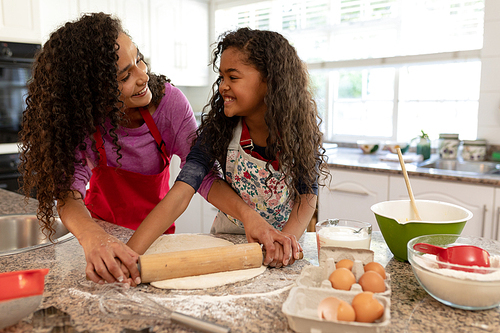 Front view of a mixed race woman in a kitchen with her young daughter at Christmas, making cookies, looking at each other
