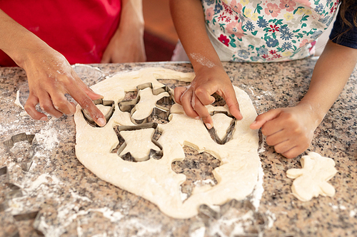 Front view mid section of a mixed race woman in a kitchen with her young daughter at Christmas, cutting out cookies