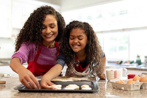 Front view of a mixed race woman in a kitchen with her young daughter at Christmas, arranging cookies on a baking tray