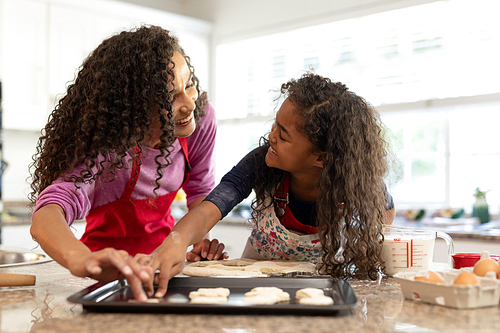 Side view of a mixed race woman in a kitchen with her young daughter at Christmas, making cookies and looking at each other