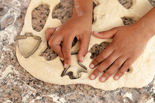 Hands of a young mixed race girl in a kitchen at Christmas, cutting out cookies