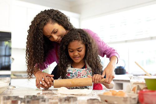 Front view of a mixed race woman in a kitchen with her young daughter at Christmas, making cookies, rolling dough together