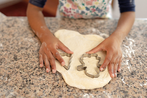 Front view mid section of a young mixed race girl in a kitchen at Christmas, making cookies and cutting out shapes