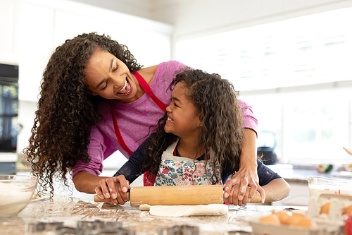Front view of a mixed race woman in a kitchen with her young daughter at Christmas, making cookies, rolling dough and looking at each other