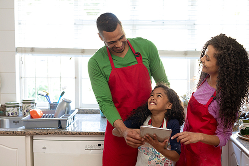 Front view of a mixed race couple with their daughter in a kitchen at Christmas, using a laptop computer