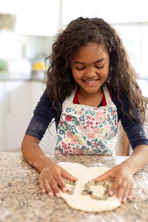 Front view of a young mixed race girl in a kitchen at Christmas, making cookies and cutting out shapes