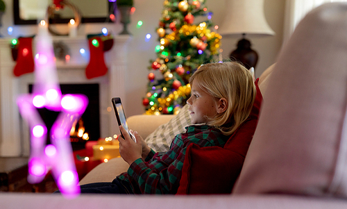 Side view of a young Caucasian boy using a tablet in the sitting room at Christmas time