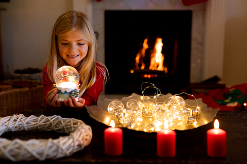 Front view of a young Caucasian girl holding a snow globe in the sitting room at Christmas time, smiling