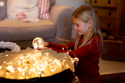 Side view of a young Caucasian girl holding a snow globe in the sitting room at Christmas time