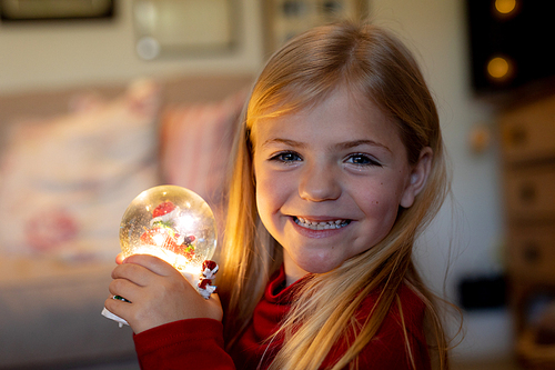 Portrait of a young Caucasian girl holding a snow globe in the sitting room at Christmas time, smiling to camera