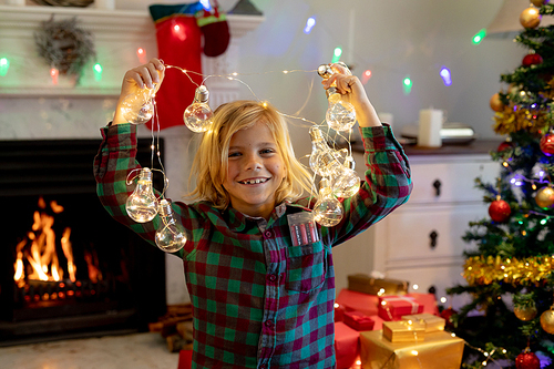 Portrait of a young Caucasian boy playing with string lights in his sitting room at Christmas time