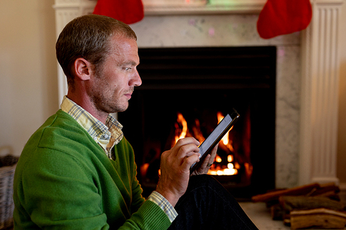 Side view of a middle aged Caucasian man using a tablet and sitting in front of the fireplace in his sitting room at Christmas time