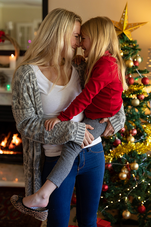 Front view of a young Caucasian woman holding her young daughter and touching noses beside the Christmas tree in their sitting room at Christmas time
