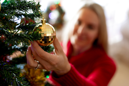 Front view of a smiling young Caucasian woman decorating the Christmas tree in her sitting room at Christmas time