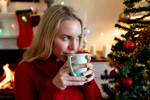 Front view of a young Caucasian woman holding a cup and drinking in her sitting room at Christmas time