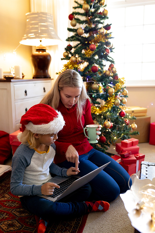 Front view of a young Caucasian woman and her young son using a laptop computer in their sitting room at Christmas time, mother is holding a cup and her son is wearing a Santa hat
