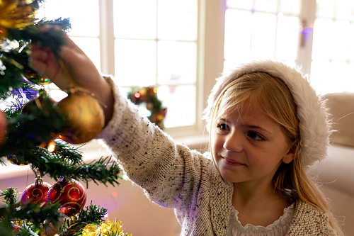 Front view close up of a young Caucasian girl decorating the Christmas tree in her sitting room at Christmas time