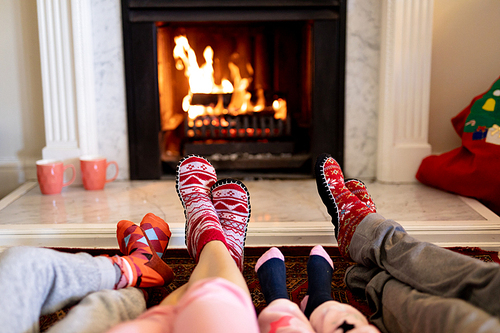 Low section of the legs of a Caucasian family lying on the floor, a couple with their young son and daughter warming their feet together in front of a fireplace in their sitting room at Christmas time