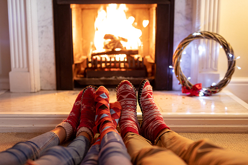 Legs of a mixed race couple with their young daughter in their sitting room at Christmas, lying on the floor by a fireplace