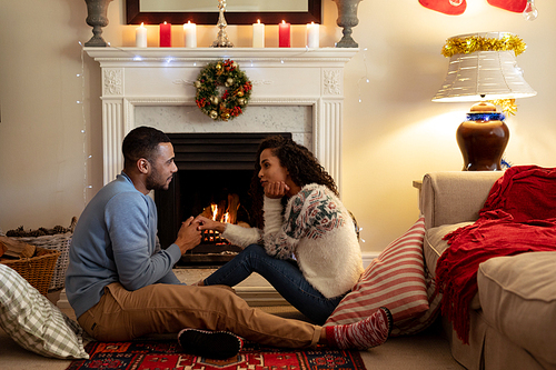 Side view of a mixed race couple in their sitting room at Christmas, facing each other holding hands
