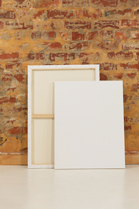 Two blank canvases leaning against a brick wall