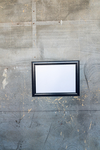 Close up of a framed blank picture hanging on a concrete wall