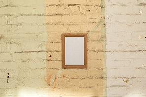 A framed blank picture hanging on a yellow brick wall