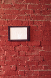 Close up of a framed blank picture hanging on a red brick wall