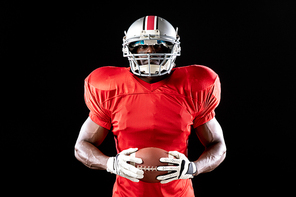 Portrait of an African American male American football player wearing a team uniform, pads and a helmet, holding a football in his hands