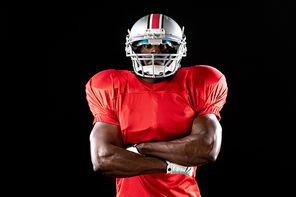 Portrait of an African American male American football player wearing a team uniform, pads and a helmet standing with arms crossed