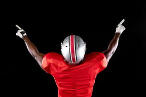 Rear view of an African American male American football player wearing a team uniform, pads, gloves and a helmet, with arms raised and pointing fingers