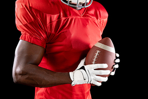 Side view mid section of an African American male American football player wearing a team uniform, pads and glaves and holding a football in his hands