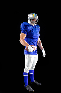 Portrait of a Caucasian male American football player wearing a team uniform, pads and a helmet, holding the ball in one hand and tunrning to camera. Vertical shot