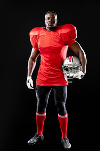 Portrait of an African American male American football player wearing a team uniform, pads and gloves, holding a helmet under his arm