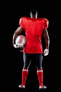 Rear view of an African American male American football player wearing a team uniform, pads and gloves, holding a helmet under his arm