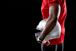 Side view mid section of an African American male American football player wearing a team uniform, pads and gloves, holding a helmet under his arm