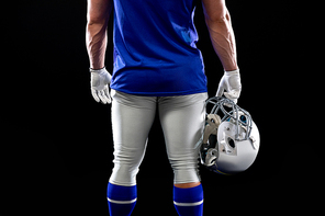 Rear view mid section of a Caucasian male American football player wearing a team uniform, pads and gloves, holding a helmet